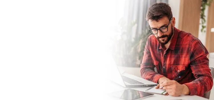 Man writing on notepad besides laptop