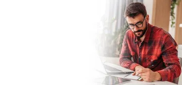 Man writing on notepad besides laptop
