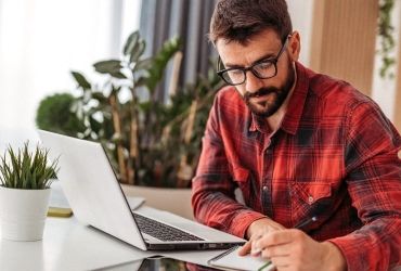 Man writing on notepad besides laptop